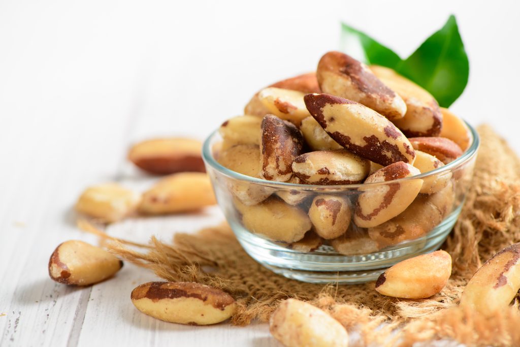 bowl with tasty brazil nuts sack space text white wooden background